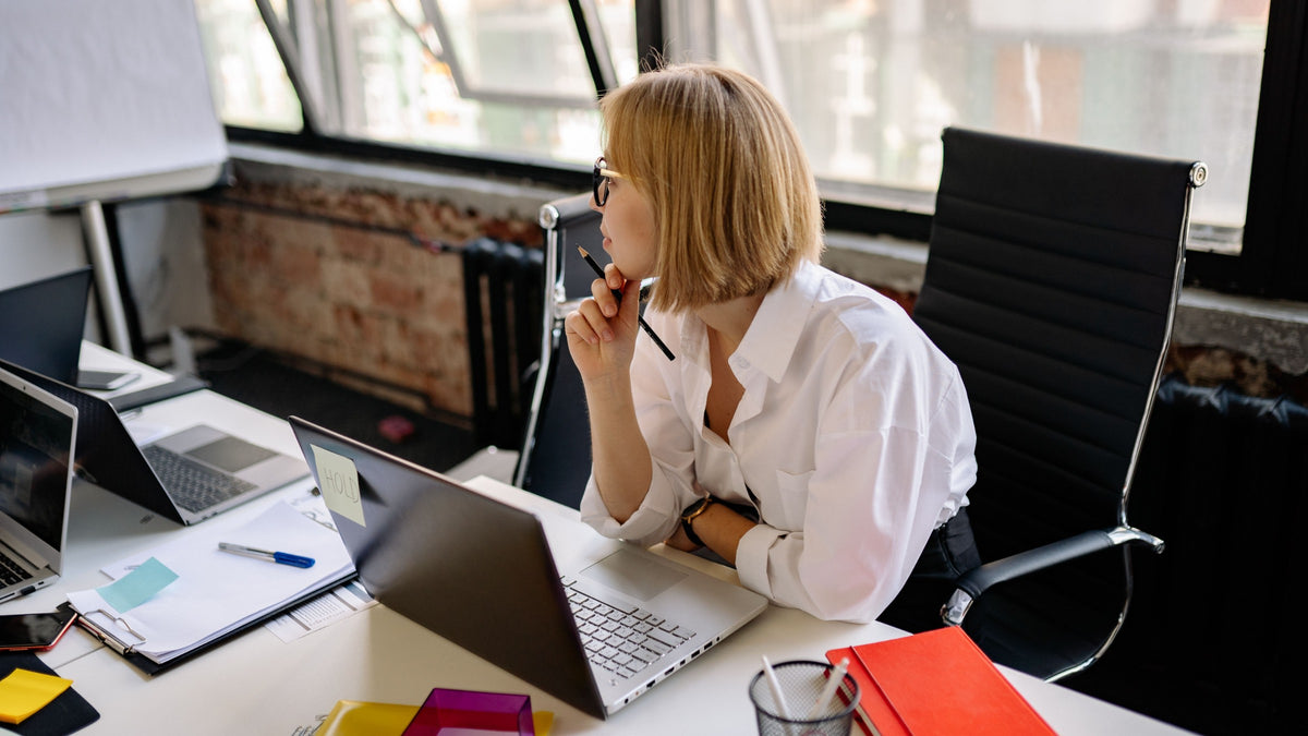 A woman at her desk with a pen at her lips, thinking